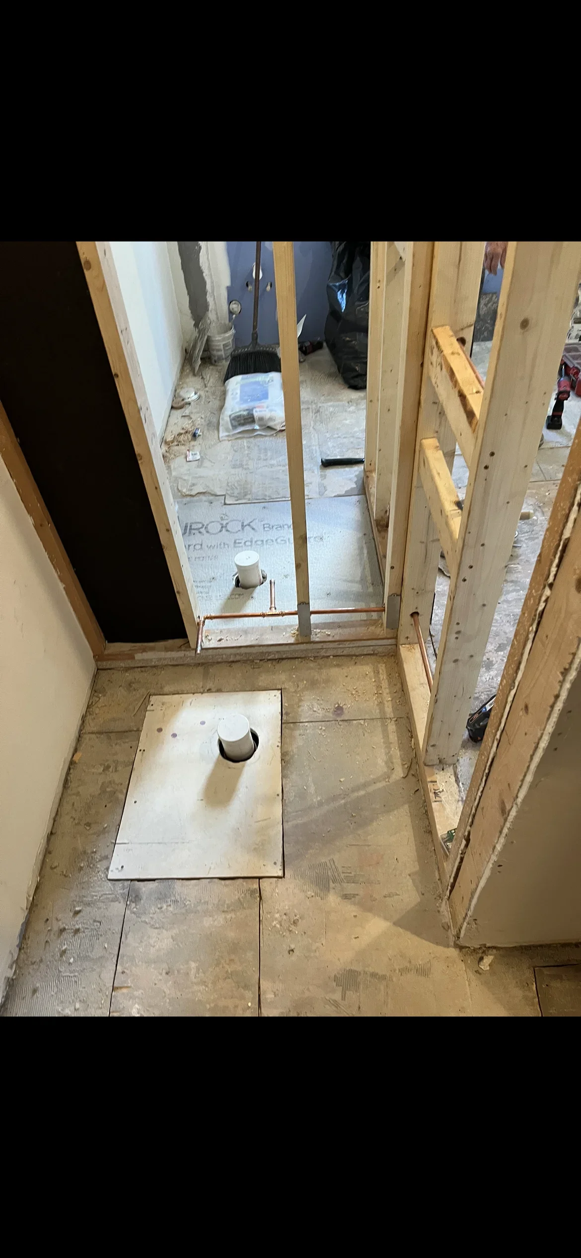 Bathroom rough-in plumbing with PVC drain lines, vent pipes, and framed walls during construction