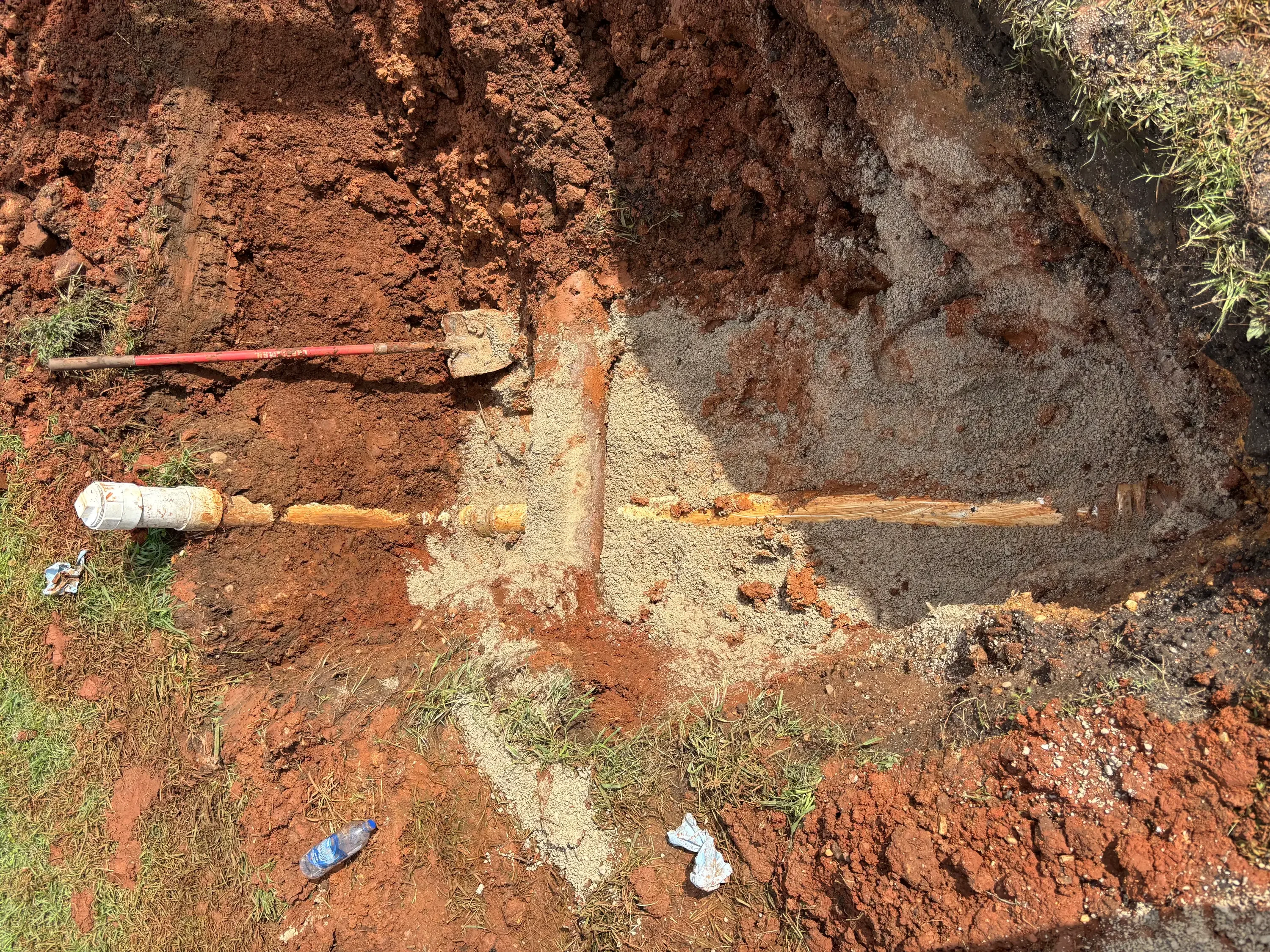 Excavated trench showing rusted underground pipe replacement with new copper line installed