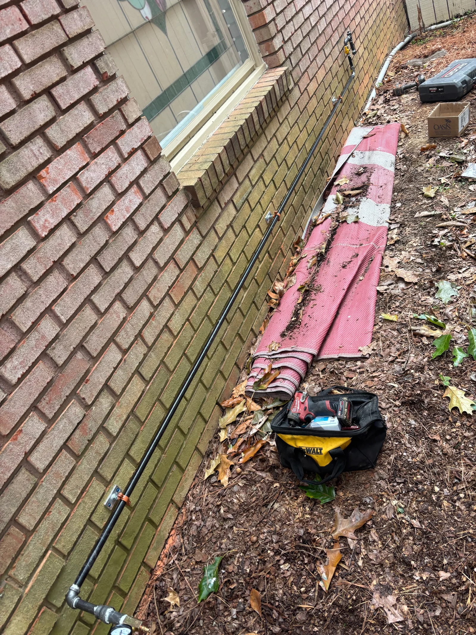 Gas line copper tubing installation along brick foundation with support straps