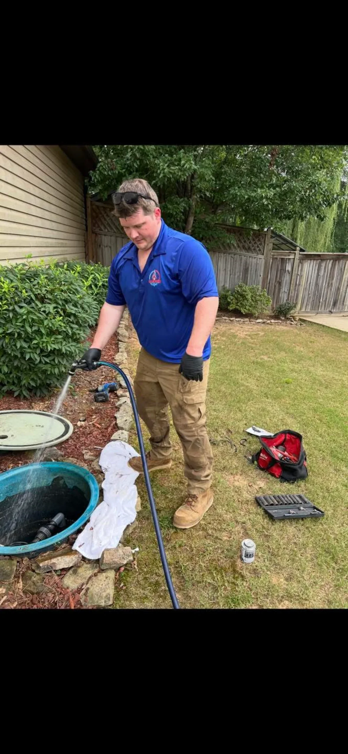 Plumber performing septic tank cleaning with hose and professional equipment in residential backyard
