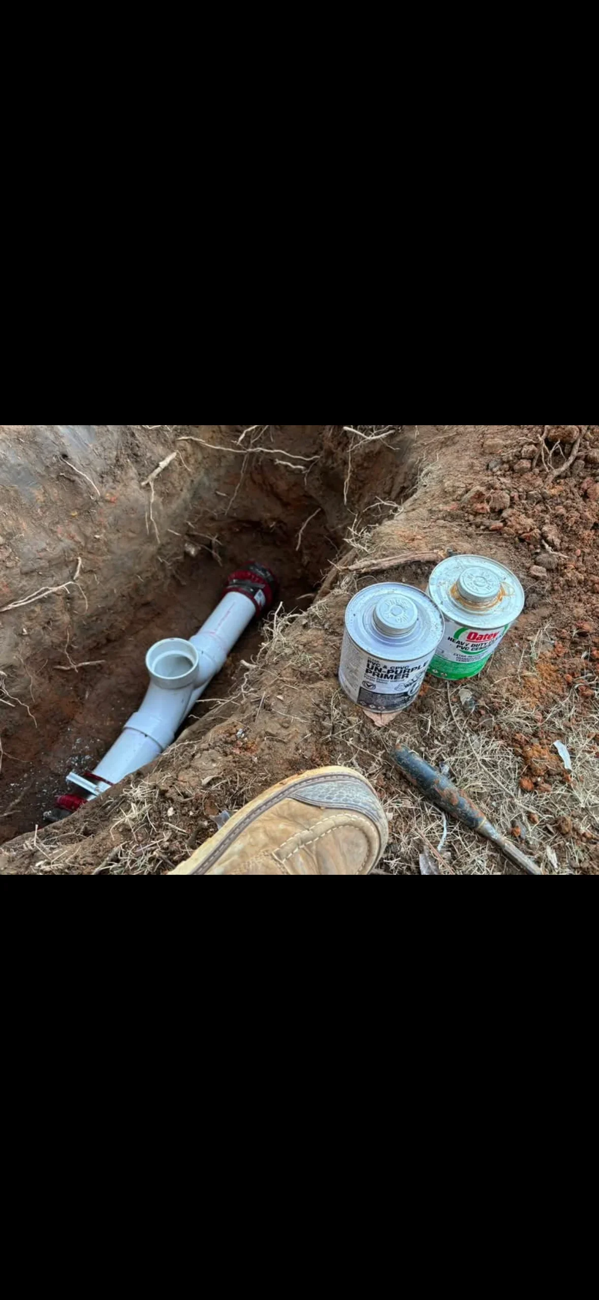 Underground PVC drainage pipe with ball valve, primer, and cement during installation in excavated trench