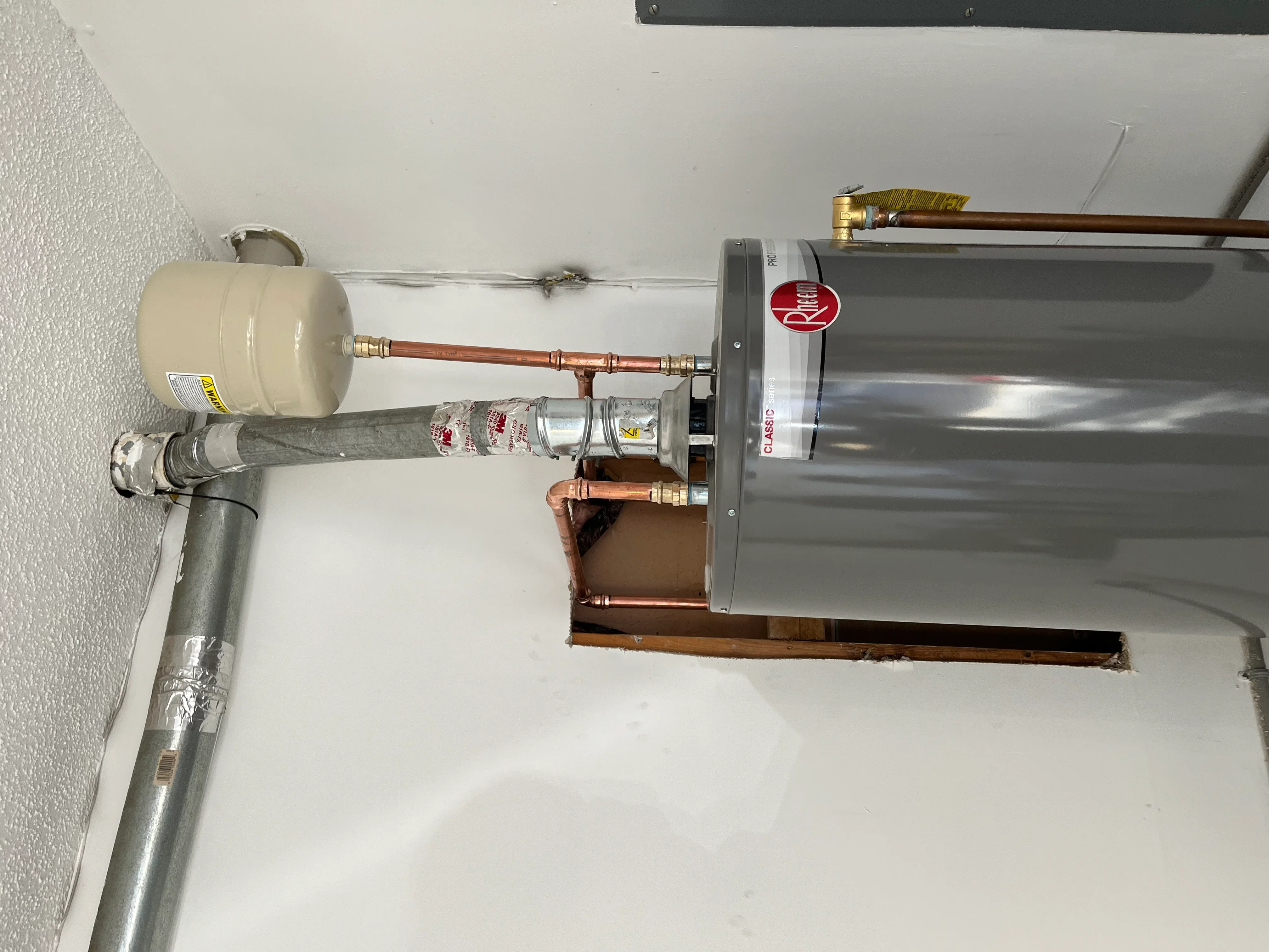 Stainless steel water heater with copper piping, expansion tank, and brass fittings installed on wall