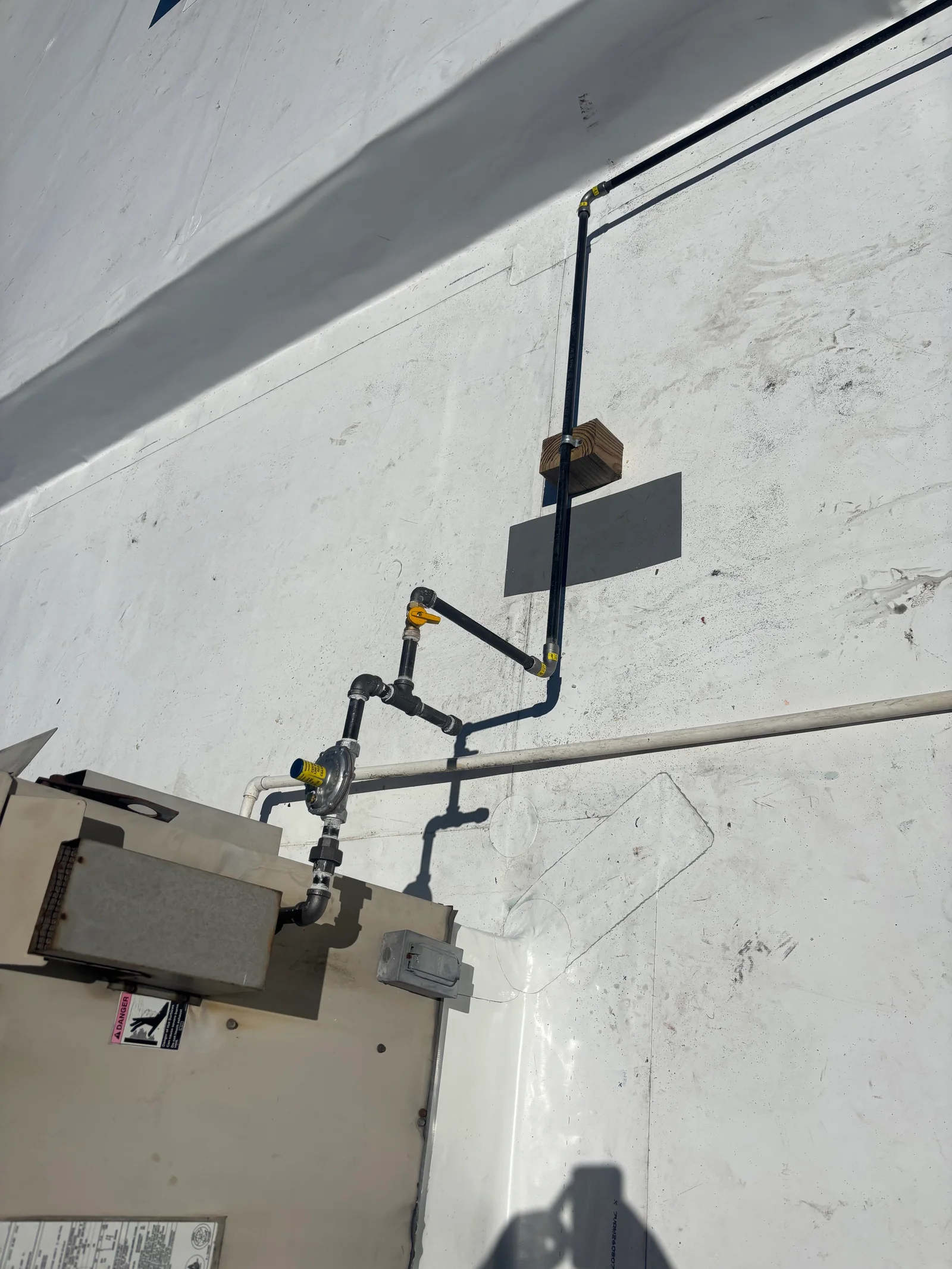 Black iron gas pipe with regulator, brackets, and yellow connectors mounted on concrete wall