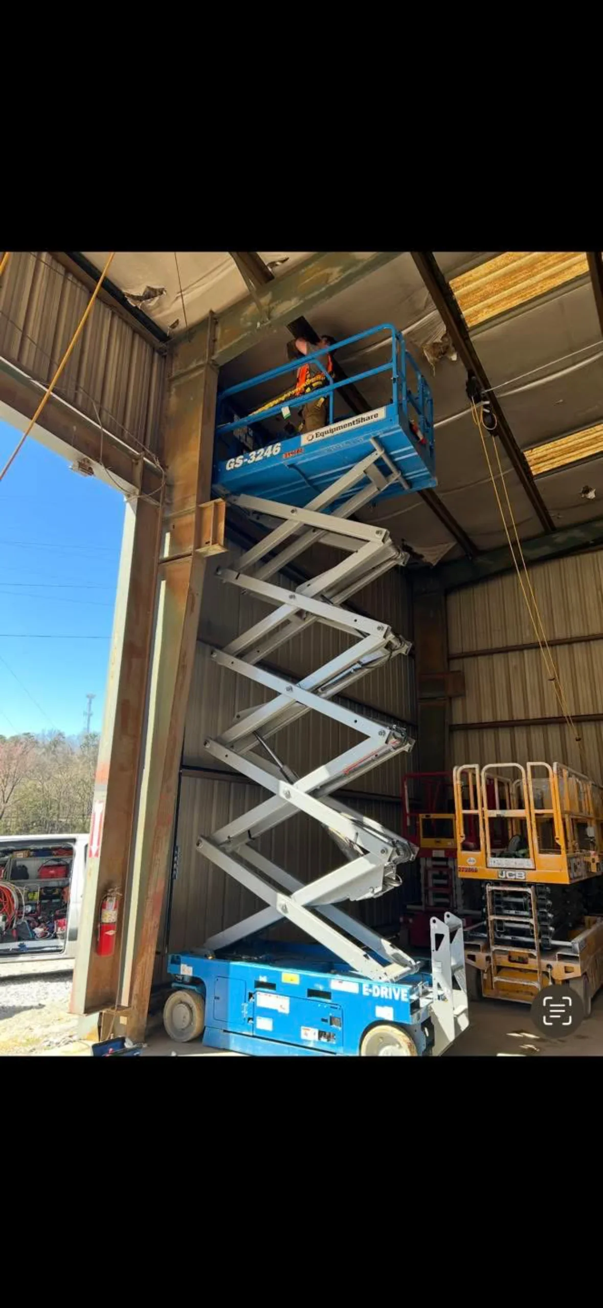 Scissor lift platform elevated to warehouse ceiling for overhead structural access and installation work