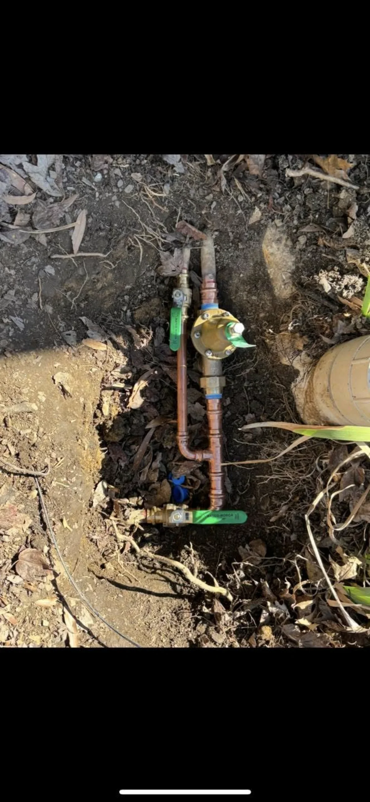 Underground copper piping with green and blue ball valves installed in excavated trench