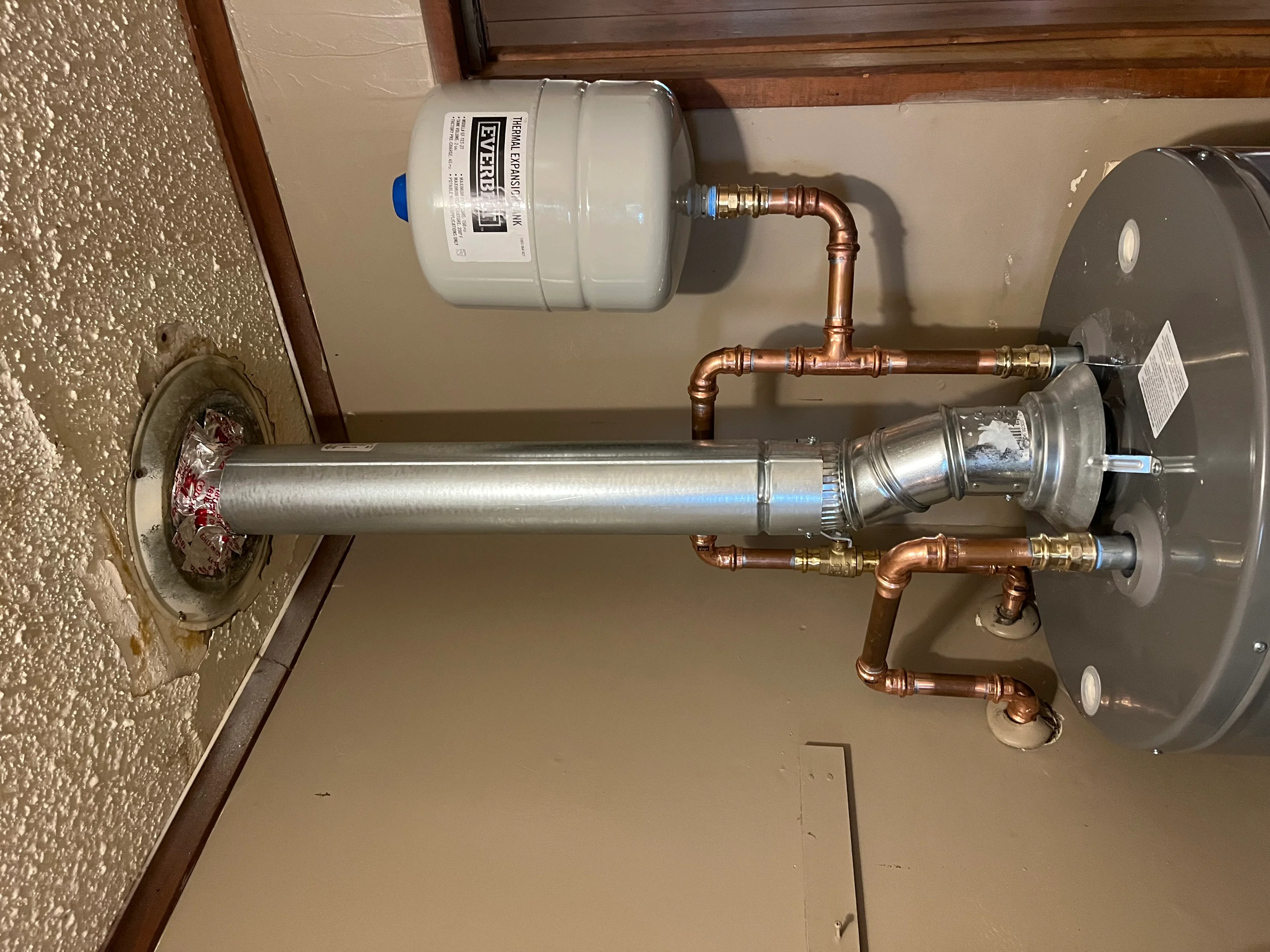 New water heater tank with copper piping, expansion tank, and brass fittings installed on wall