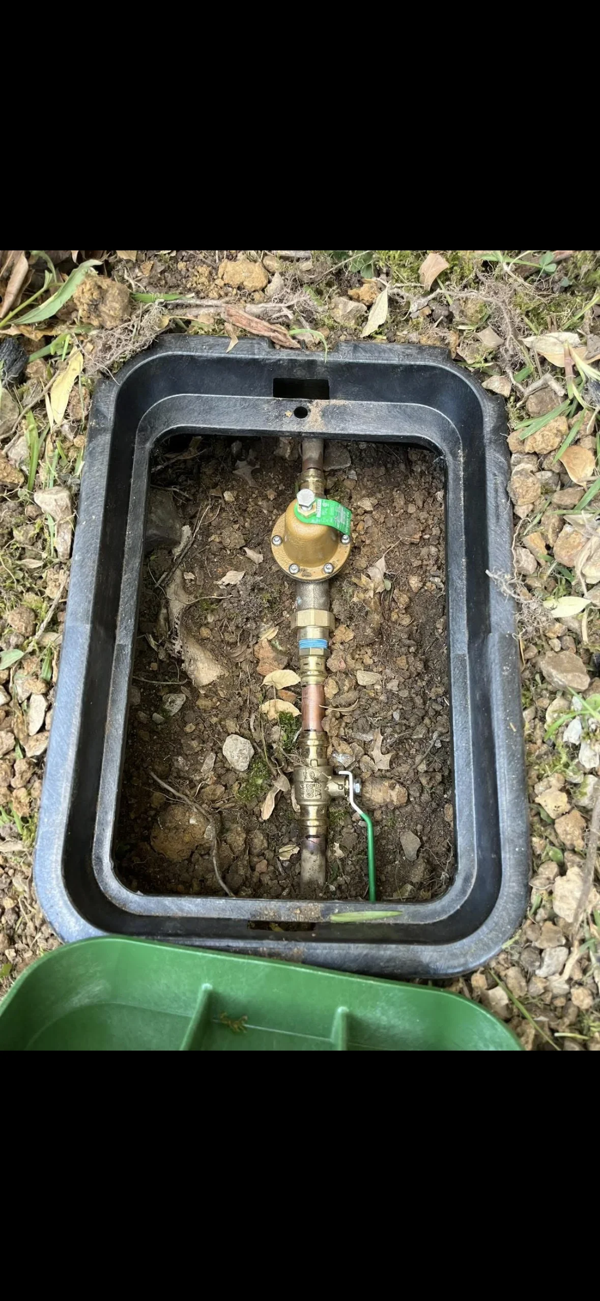 Brass water main valve with green handle installed in concrete underground utility box