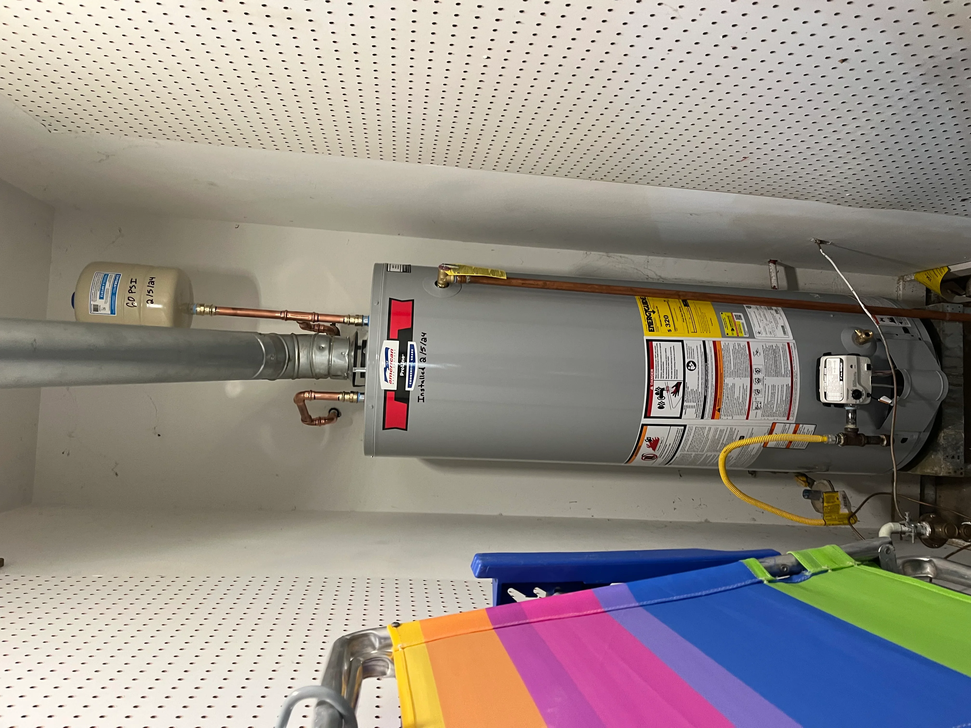 Gas water heater with copper lines, red valve, and yellow gas connector installed against white wall