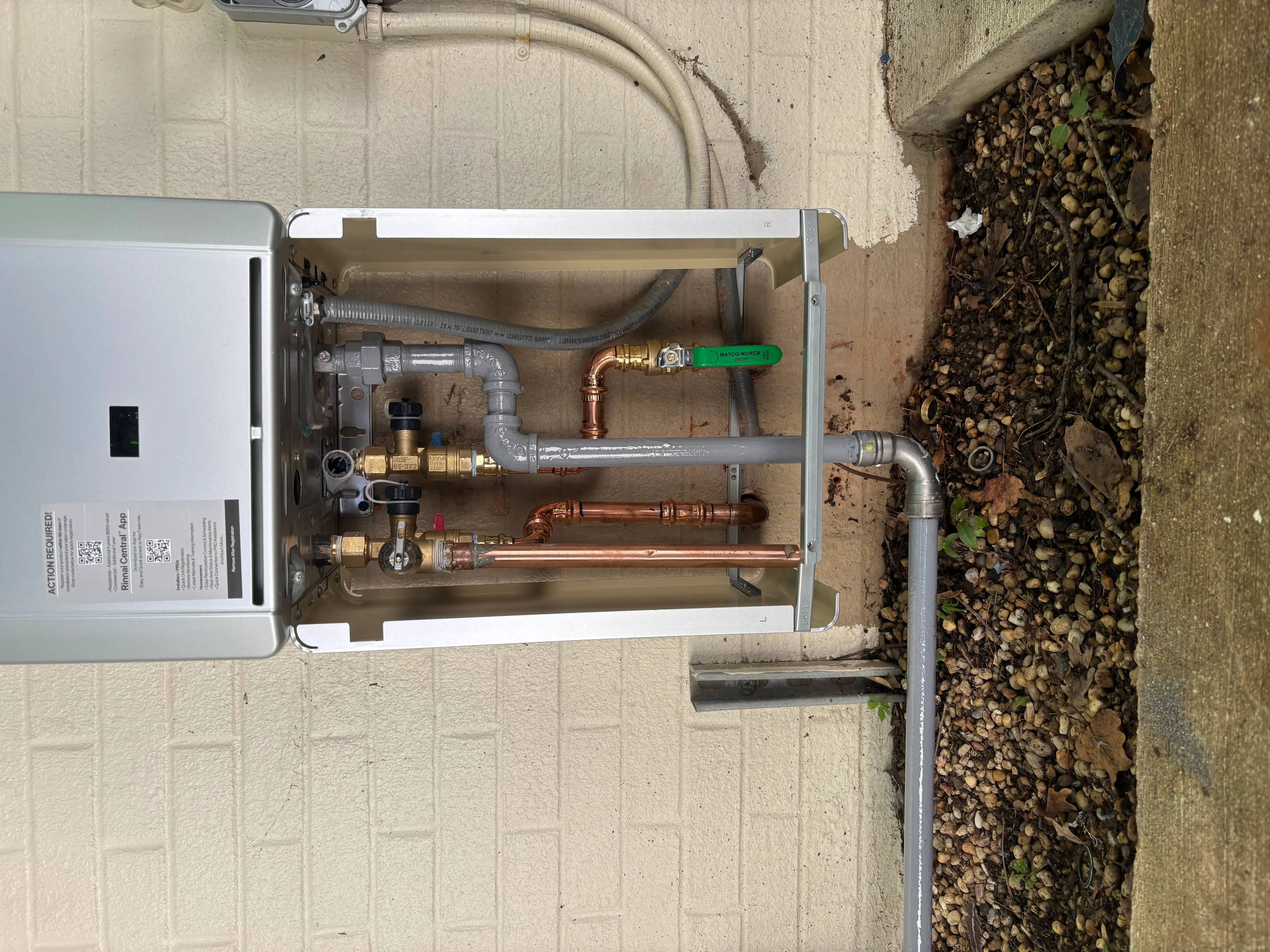 Tankless water heater with copper piping, brass valves, and green isolation valve installed on exterior wall