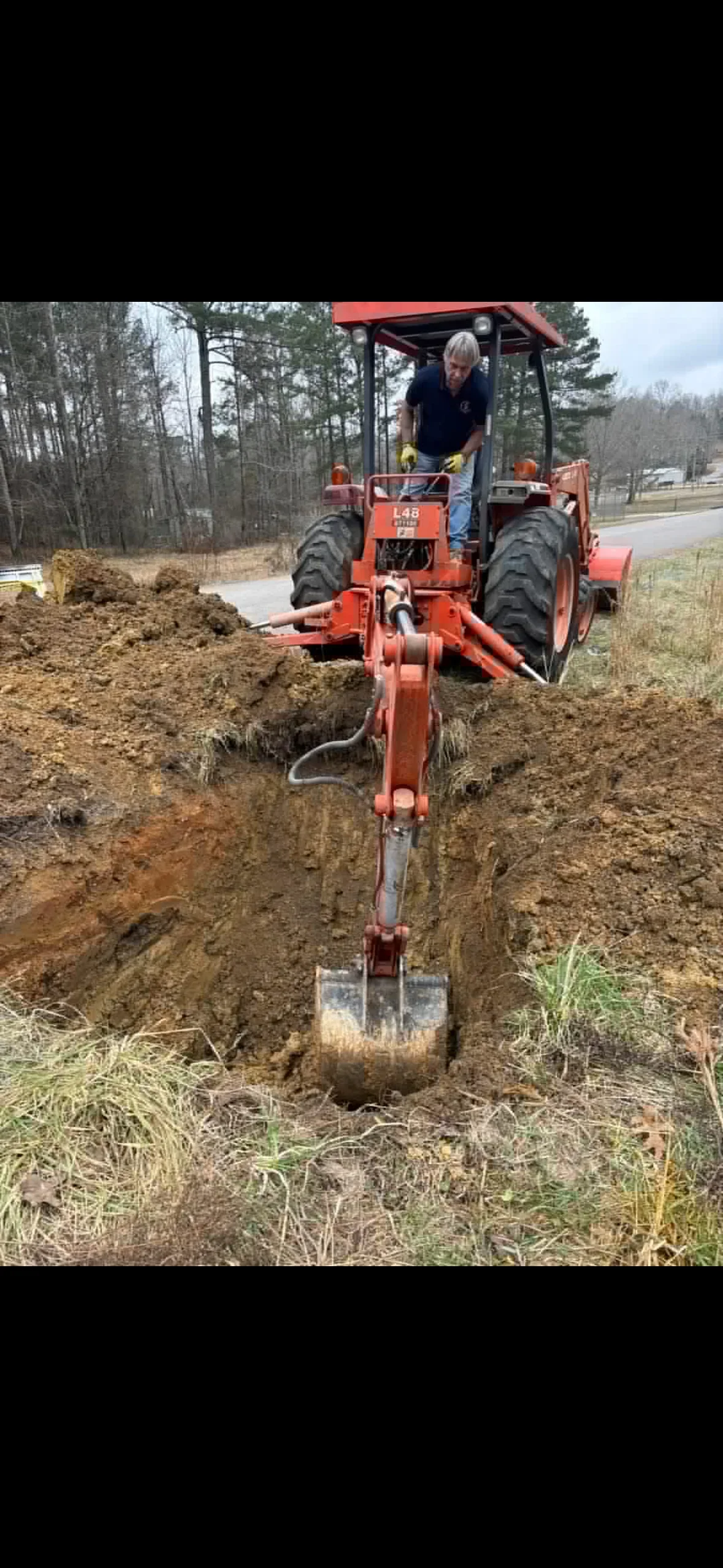 Compact loader with bucket excavating soil for septic system installation