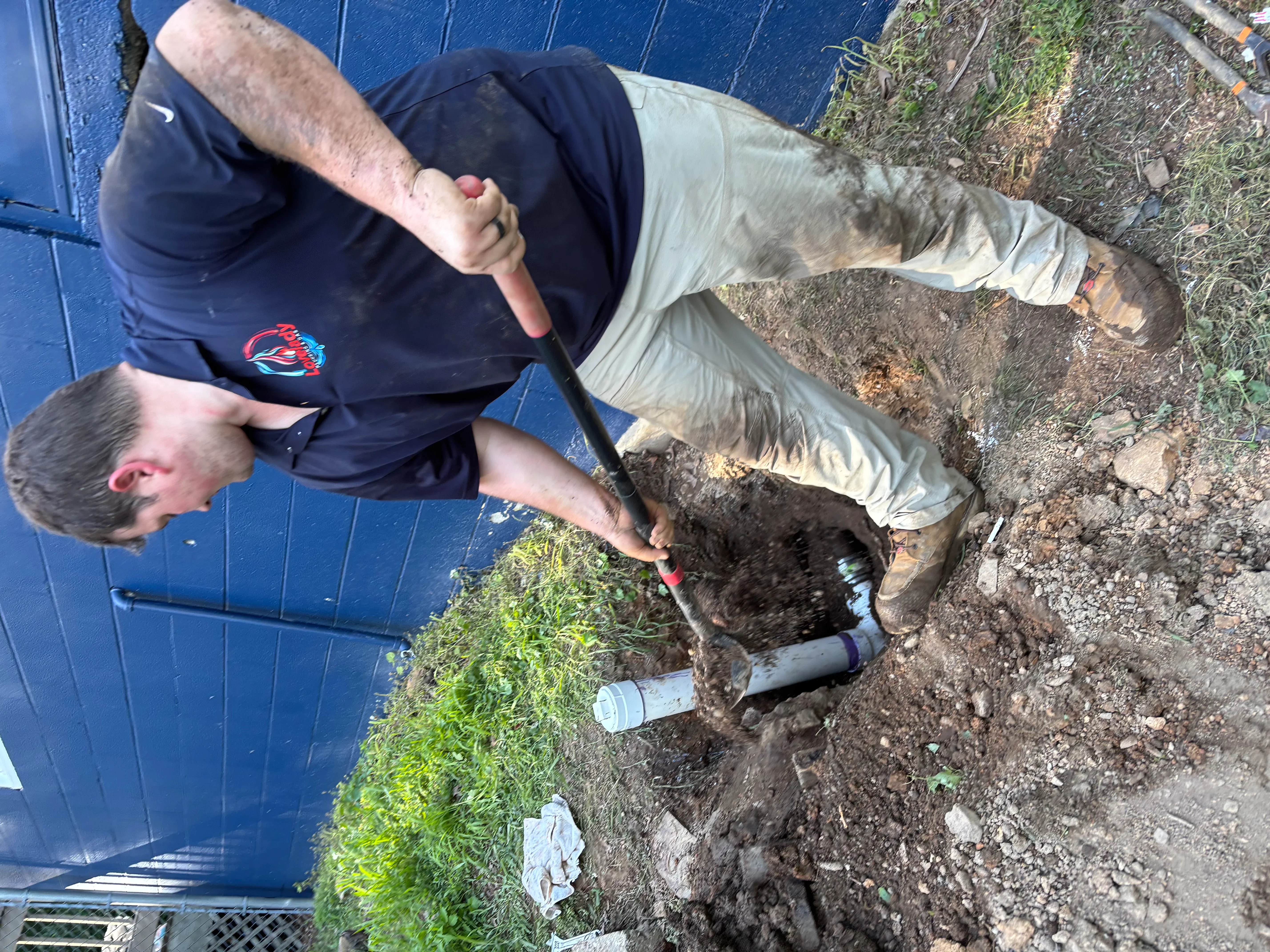 Plumber excavating underground drain line in residential yard with hand tools