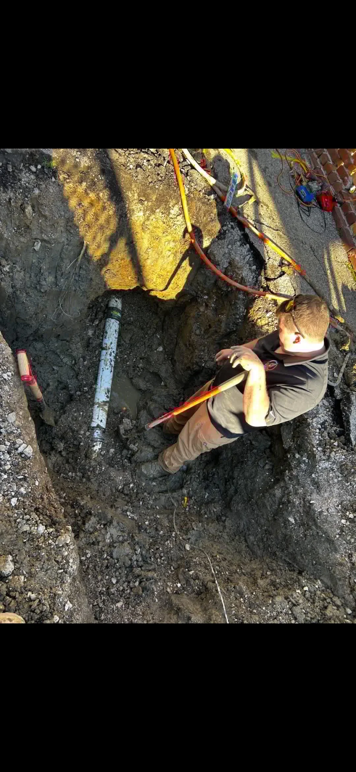 Technician installing underground water lines with yellow conduit and color-coded pipes in excavated trench