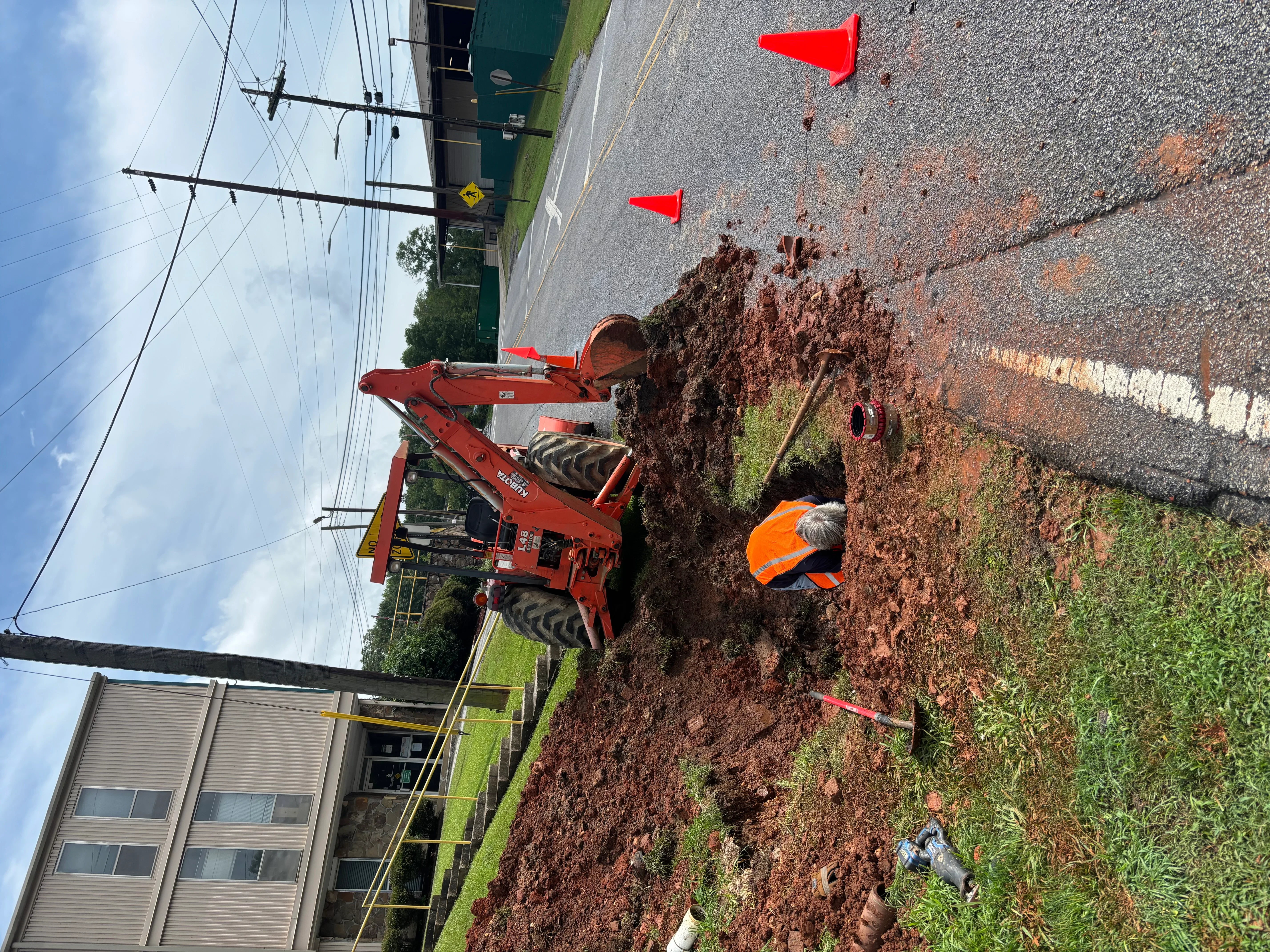 Red excavator digging residential lot with exposed soil and underground utility access