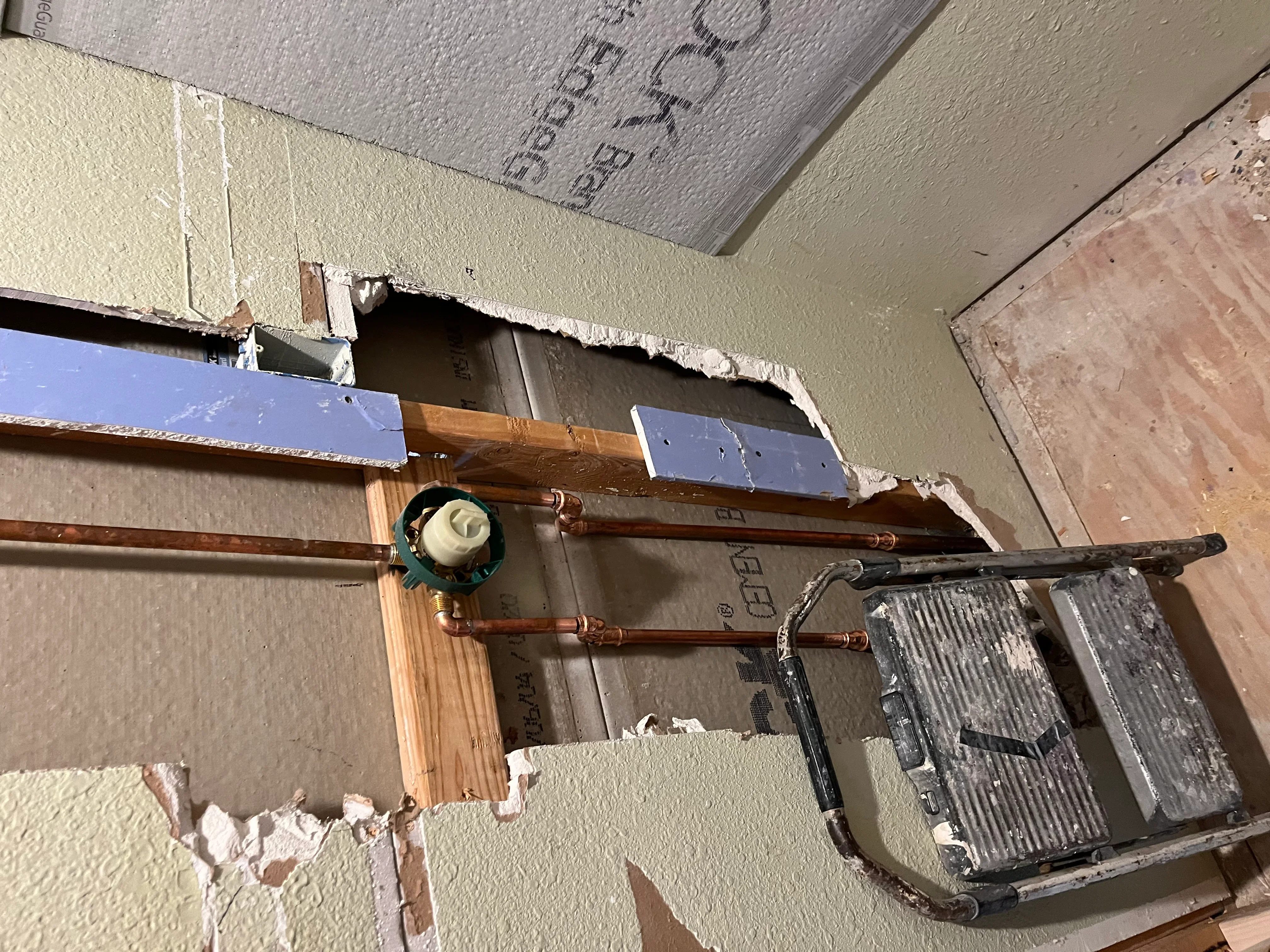 Copper pipe installation with soldered joints, shut-off valve, and blue insulation wrapping in wall framing