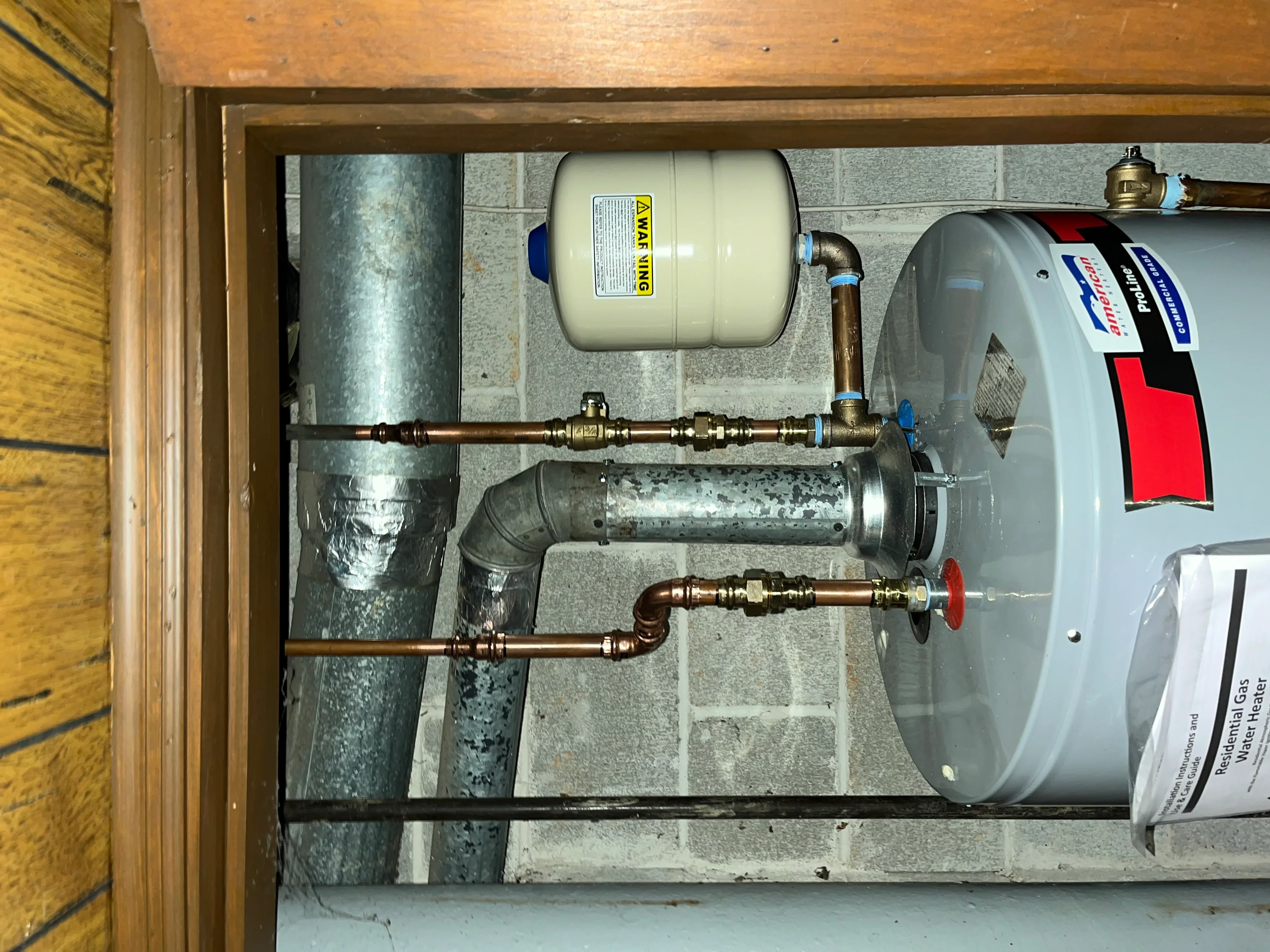Water heater tank with expansion tank, copper piping, brass fittings, and pressure relief valve installed in utility closet